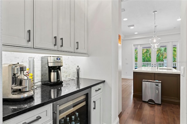 bar featuring dark wood finished floors, decorative backsplash, wine cooler, ornamental molding, and a sink