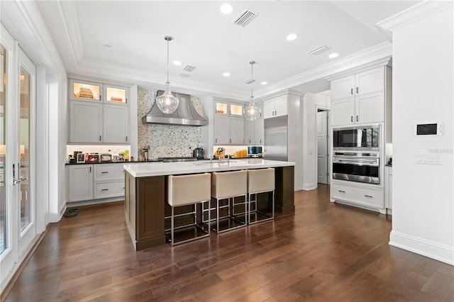 kitchen featuring wall chimney range hood, visible vents, ornamental molding, and built in appliances