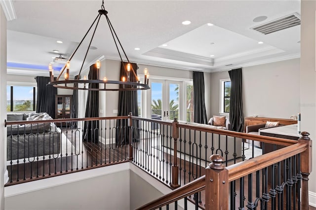 hallway with visible vents, a raised ceiling, a wealth of natural light, and an upstairs landing