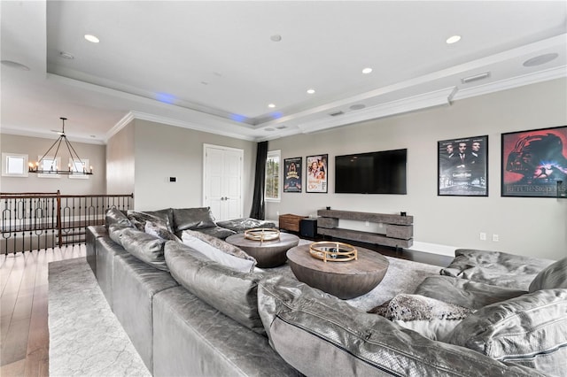 living area with a raised ceiling, ornamental molding, wood finished floors, an inviting chandelier, and recessed lighting