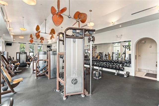 exercise room with arched walkways, visible vents, vaulted ceiling, and baseboards