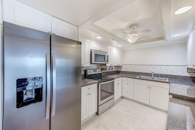 kitchen featuring appliances with stainless steel finishes, a tray ceiling, sink, and white cabinets