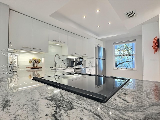 kitchen with appliances with stainless steel finishes, white cabinetry, decorative backsplash, light stone counters, and a raised ceiling