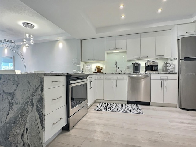 kitchen featuring sink, appliances with stainless steel finishes, a tray ceiling, white cabinets, and light wood-type flooring