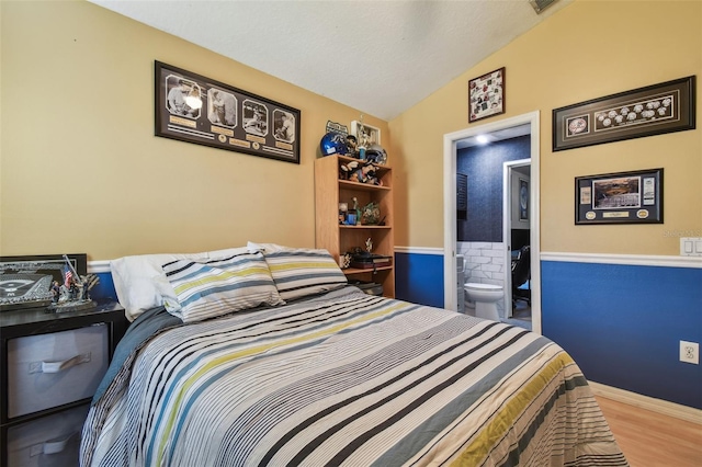 bedroom with hardwood / wood-style flooring, vaulted ceiling, and ensuite bath