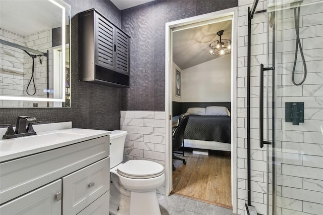 bathroom featuring a shower with door, vanity, tile walls, and toilet