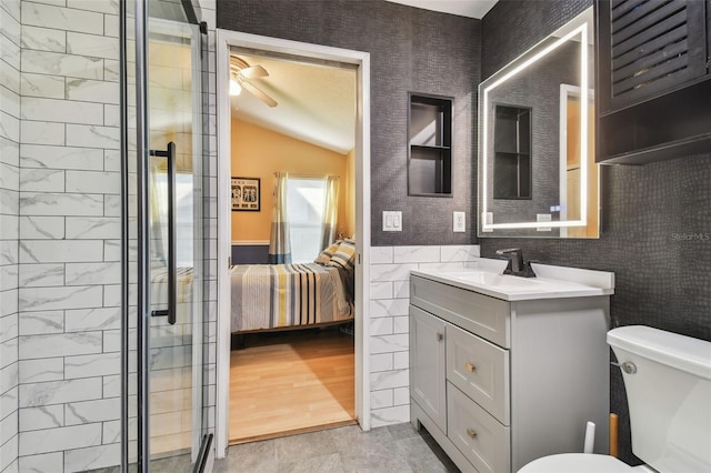 bathroom with toilet, tile walls, vanity, a shower with door, and ceiling fan