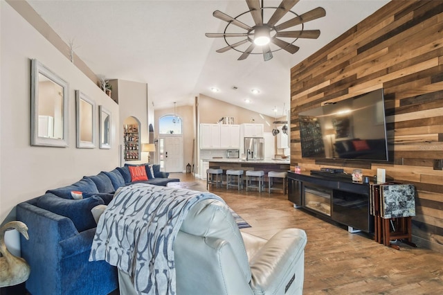 living room featuring ceiling fan, lofted ceiling, wooden walls, and light hardwood / wood-style floors