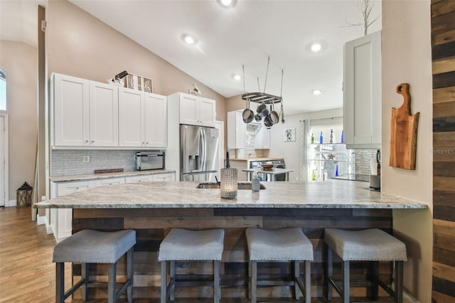 kitchen with sink, a breakfast bar, white cabinets, and stainless steel refrigerator with ice dispenser