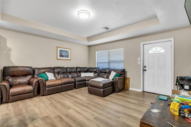 living room with light wood finished floors, visible vents, baseboards, and a tray ceiling