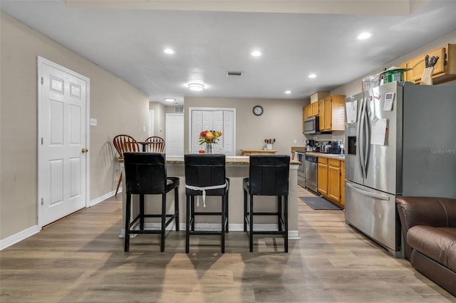 kitchen featuring visible vents, a kitchen island, wood finished floors, stainless steel appliances, and a breakfast bar area