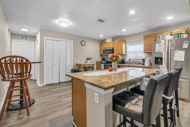 kitchen featuring visible vents, stainless steel appliances, a kitchen bar, and light wood-type flooring