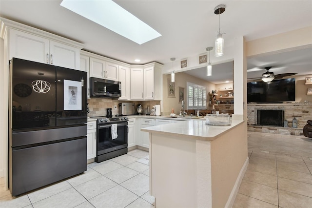 kitchen with light tile patterned flooring, a stone fireplace, white cabinetry, kitchen peninsula, and stainless steel appliances