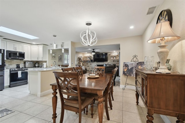 tiled dining room with ceiling fan with notable chandelier and a skylight