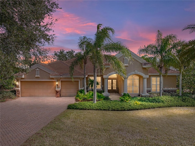 mediterranean / spanish house with an attached garage, stucco siding, french doors, a tile roof, and decorative driveway