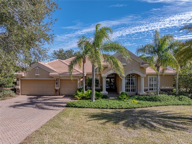 mediterranean / spanish house with a garage, decorative driveway, a tiled roof, and stucco siding