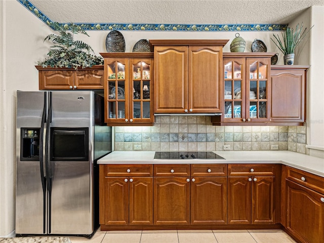 kitchen featuring a textured ceiling, black electric cooktop, light countertops, stainless steel refrigerator with ice dispenser, and decorative backsplash