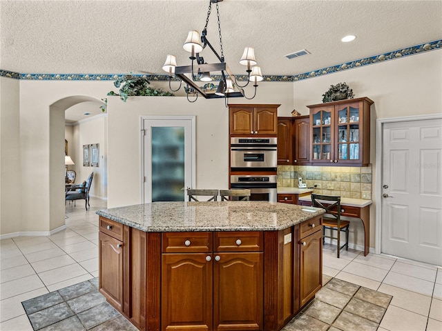 kitchen with arched walkways, light tile patterned flooring, a kitchen island, visible vents, and decorative backsplash