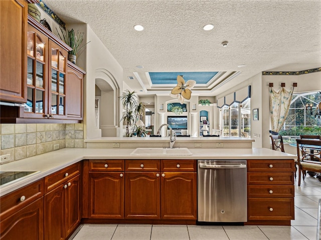 kitchen featuring a raised ceiling, light countertops, glass insert cabinets, a sink, and dishwasher