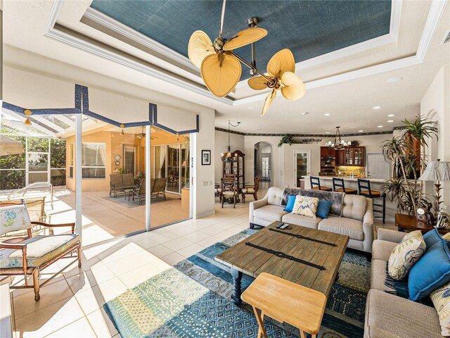 living room featuring arched walkways, crown molding, a raised ceiling, light tile patterned flooring, and ceiling fan with notable chandelier