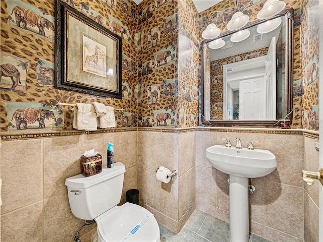 bathroom with tile patterned flooring, toilet, a wainscoted wall, tile walls, and wallpapered walls