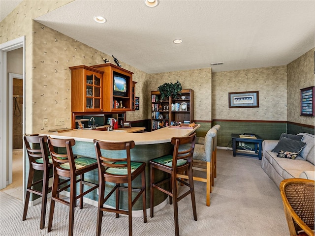 interior space featuring wallpapered walls, wet bar, light colored carpet, and wainscoting