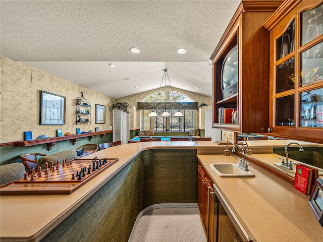 bar featuring decorative light fixtures, lofted ceiling, a sink, a textured ceiling, and wallpapered walls