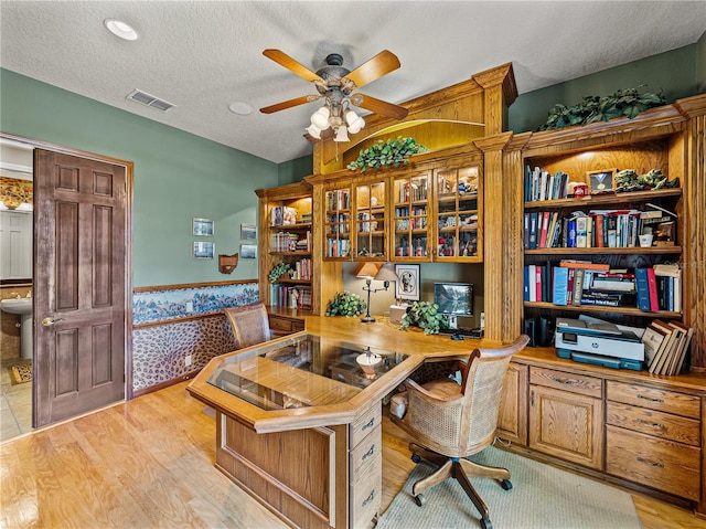 office featuring light wood-style floors, visible vents, a textured ceiling, and wainscoting