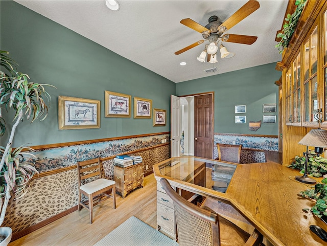 office area with a wainscoted wall, visible vents, a ceiling fan, a textured ceiling, and wood finished floors