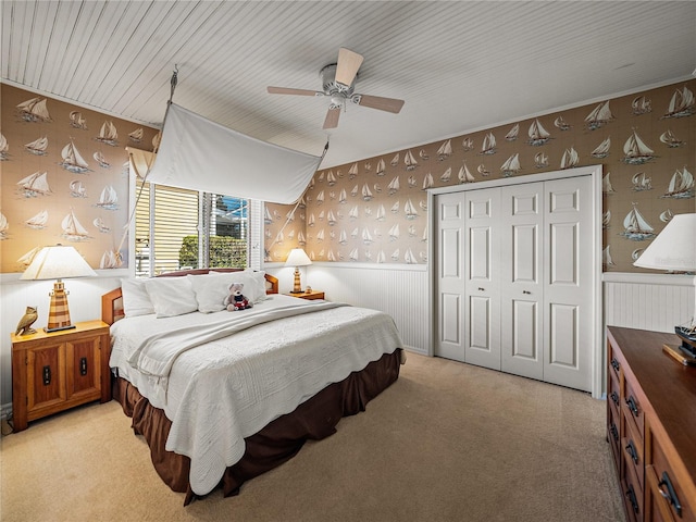 bedroom featuring wallpapered walls, a ceiling fan, light colored carpet, a wainscoted wall, and a closet