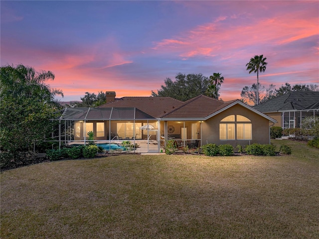 back of property at dusk featuring a yard, a chimney, a patio area, glass enclosure, and an outdoor pool