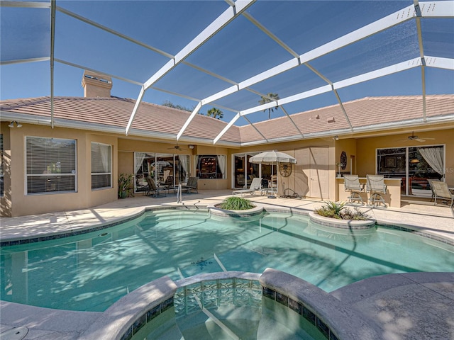 view of pool with a ceiling fan, glass enclosure, a pool with connected hot tub, and a patio area