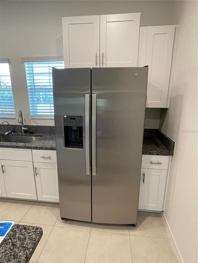 kitchen with stainless steel refrigerator with ice dispenser, sink, light tile patterned floors, dark stone countertops, and white cabinets