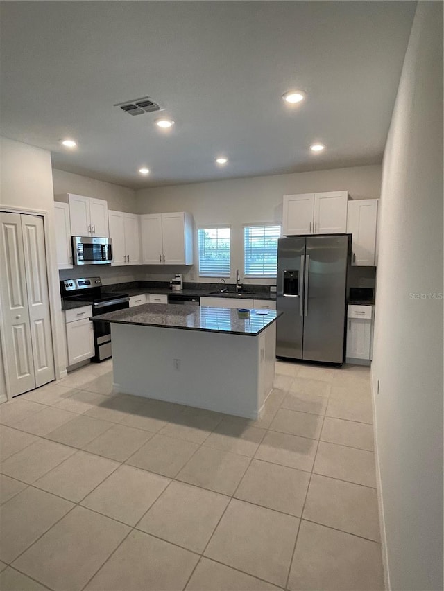 kitchen with sink, light tile patterned floors, appliances with stainless steel finishes, white cabinets, and a kitchen island