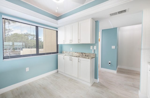 kitchen with white cabinetry, ornamental molding, light stone countertops, and light hardwood / wood-style flooring