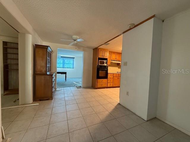 interior space featuring light tile patterned floors, a textured ceiling, oven, and ceiling fan