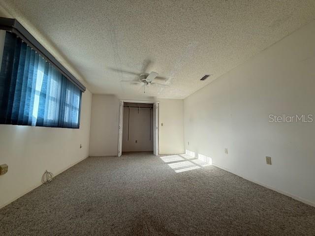 carpeted empty room with ceiling fan and a textured ceiling