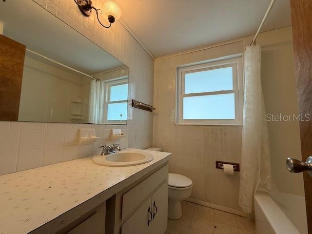 full bathroom featuring tasteful backsplash, tile walls, vanity, toilet, and shower / bath combo with shower curtain