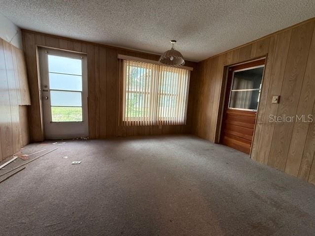 empty room featuring carpet flooring, a textured ceiling, and wood walls