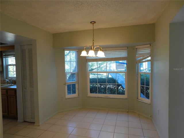 unfurnished dining area with light tile patterned flooring, a wealth of natural light, a notable chandelier, and a textured ceiling