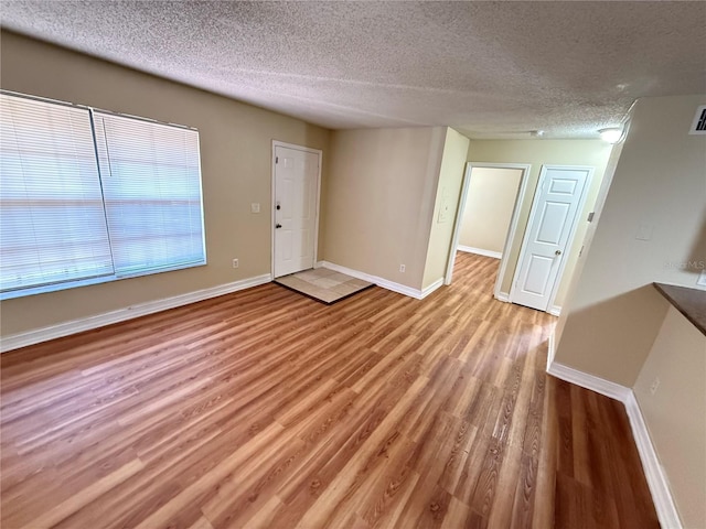 interior space featuring light wood-style floors, visible vents, a textured ceiling, and baseboards