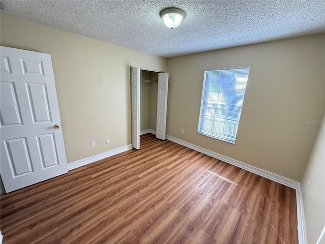 unfurnished bedroom with a textured ceiling, a closet, wood finished floors, and baseboards