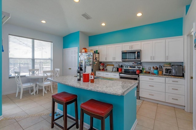 kitchen with stainless steel appliances, white cabinetry, a kitchen island with sink, and light tile patterned floors