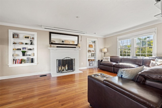 living room featuring crown molding, a brick fireplace, built in shelves, and wood-type flooring