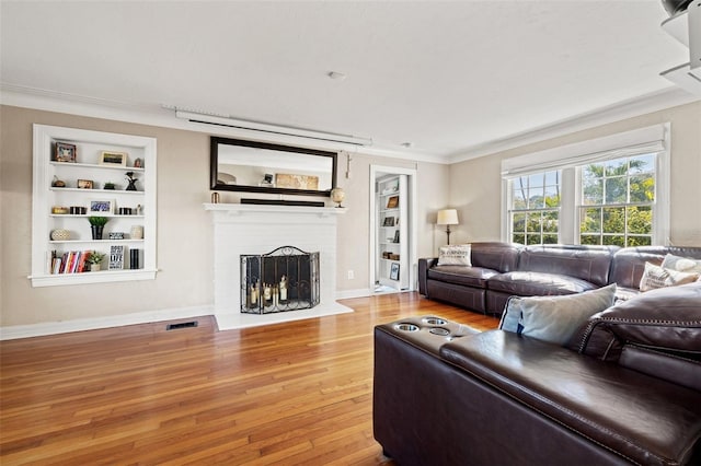 living room with ornamental molding, wood-type flooring, built in features, and a fireplace