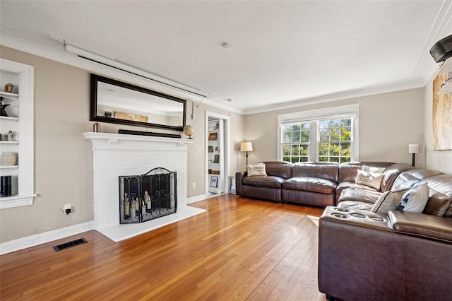 living room featuring wood-type flooring, built in features, crown molding, and a fireplace