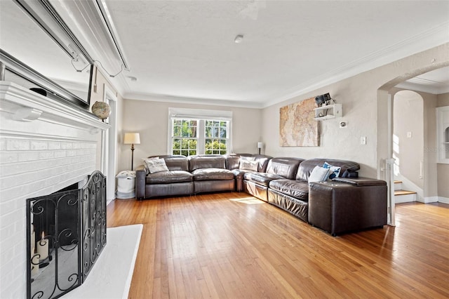 living room featuring crown molding, wood-type flooring, and a brick fireplace