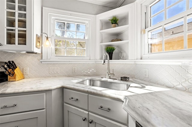 kitchen featuring sink, backsplash, ornamental molding, and light stone countertops