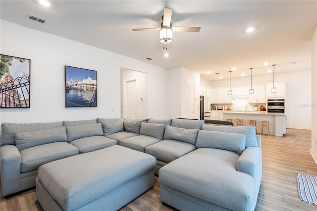 living room with ceiling fan, sink, and light hardwood / wood-style floors