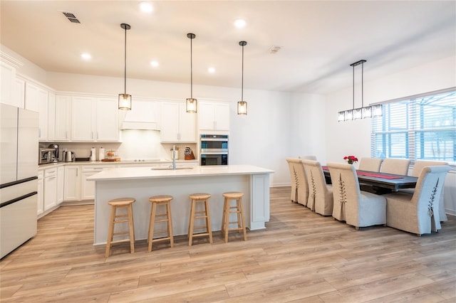 kitchen with white fridge, pendant lighting, a center island with sink, and double oven